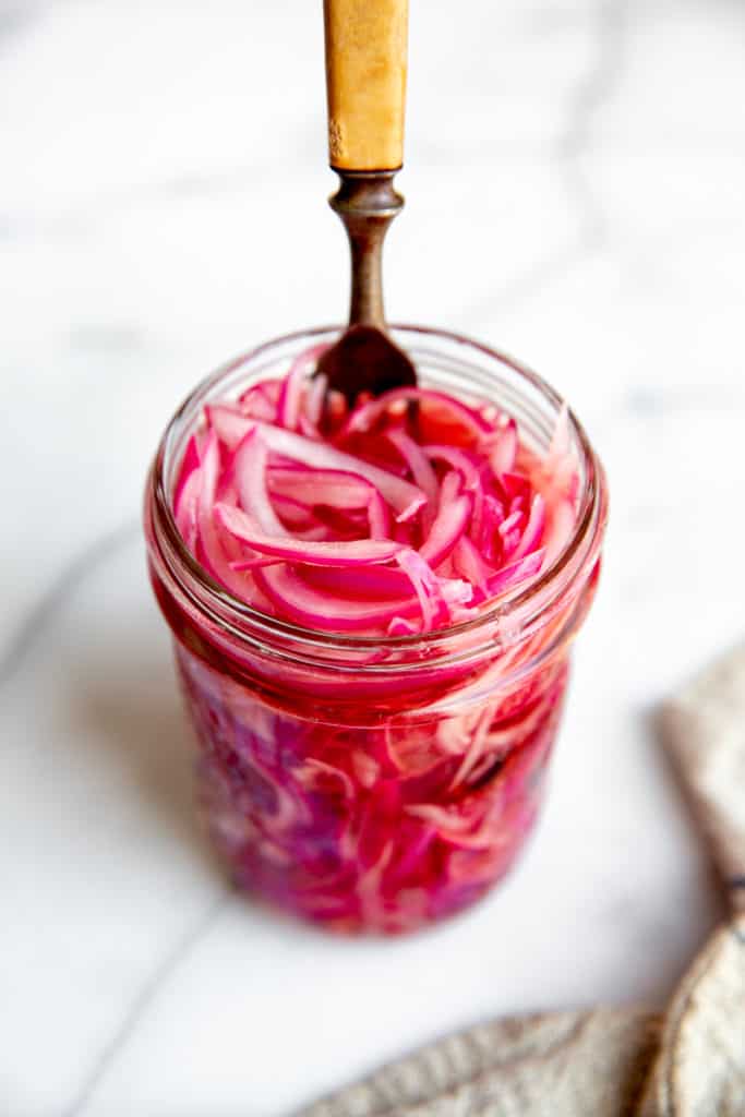 A jar of quick pickled red onions with a fork sticking out the top. 