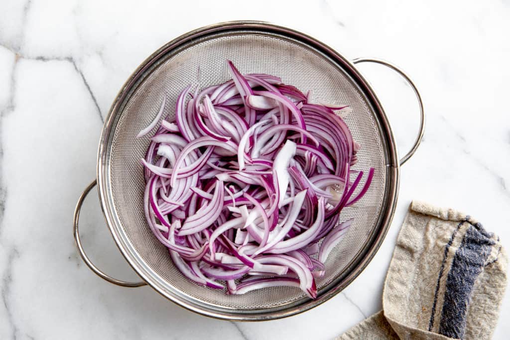 Process shot showing the sliced red onions in a strainer. 