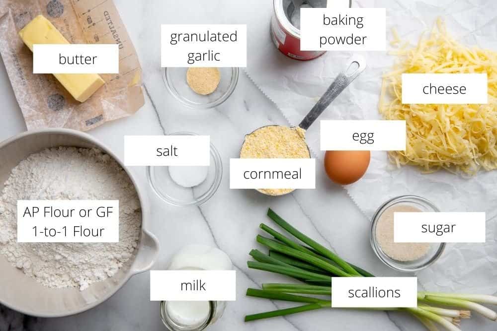 All of the ingredients for the cheese scones recipe arranged on a marble surface with labels.
