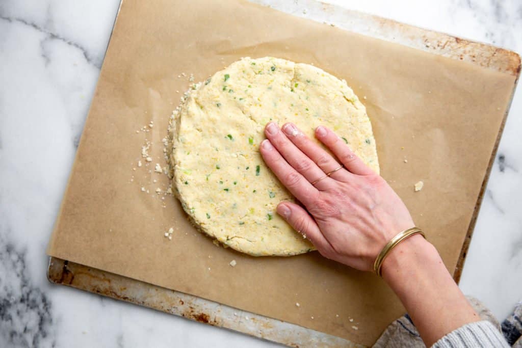 A hand pressing the cheese scone dough into a half-inch round. 