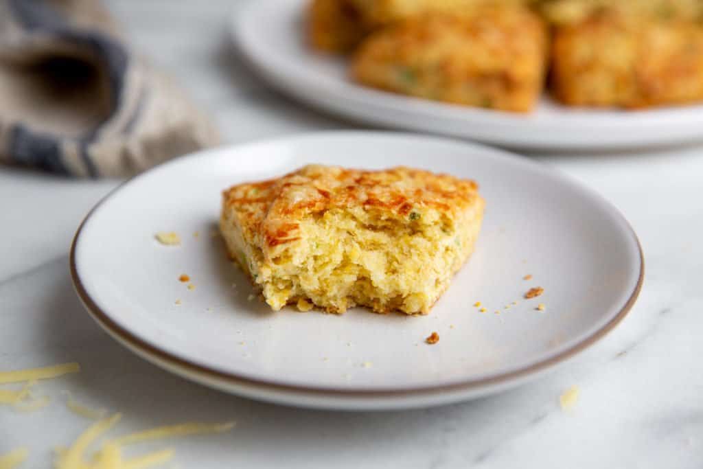 A cheese scone on a plate with a bite taken out. 