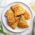 Savory cheese scones on a plate with green onions and shredded cheddar alongside.