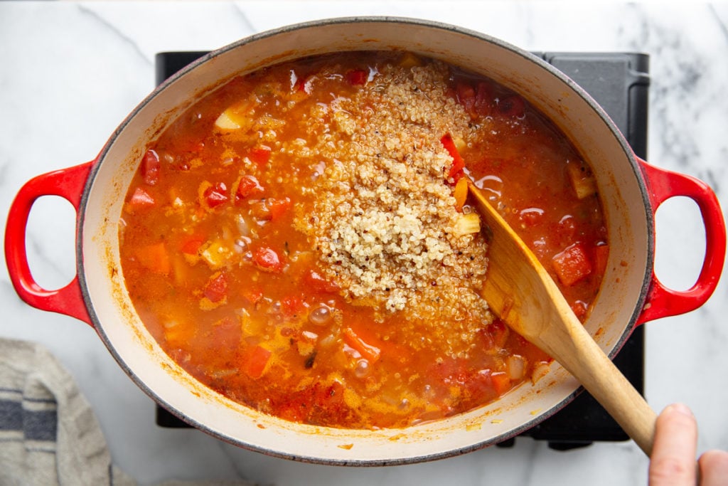 A hand stirring cooked quinoa into the chili. 