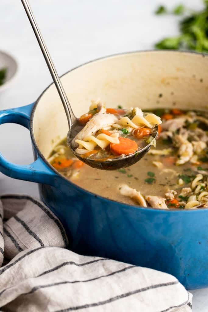 A ladle scooping homemade chicken soup from a pot. 