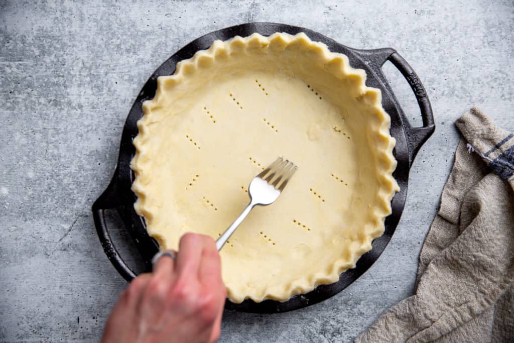 A hand pricking an unbaked pie crust with a fork. 