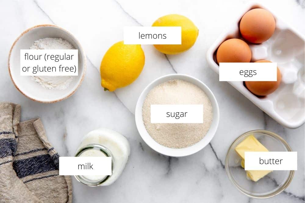 All of the ingredients for the lemon pudding cakes arranged on a marble surface with labels. 