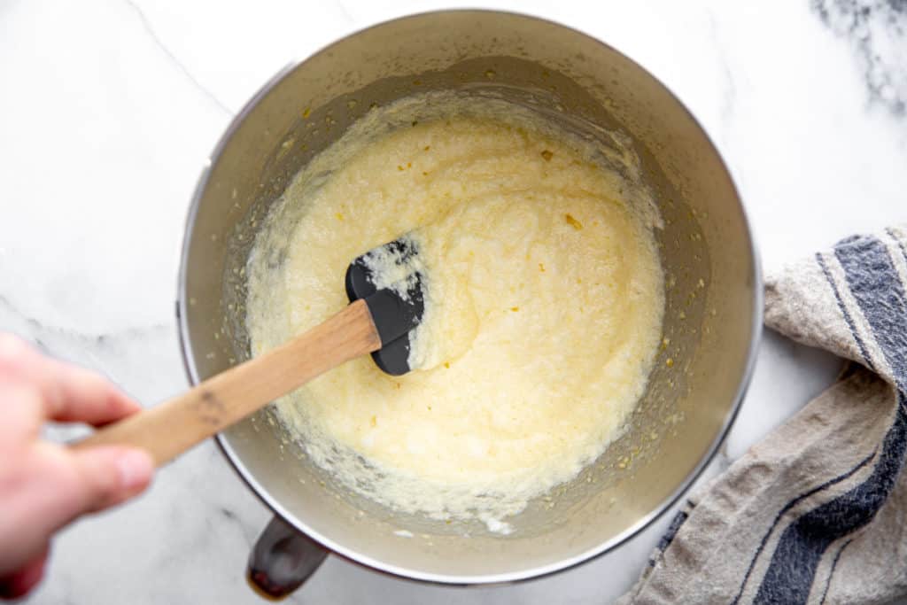 A hand stirring the lemon pudding cake batter in a bowl.