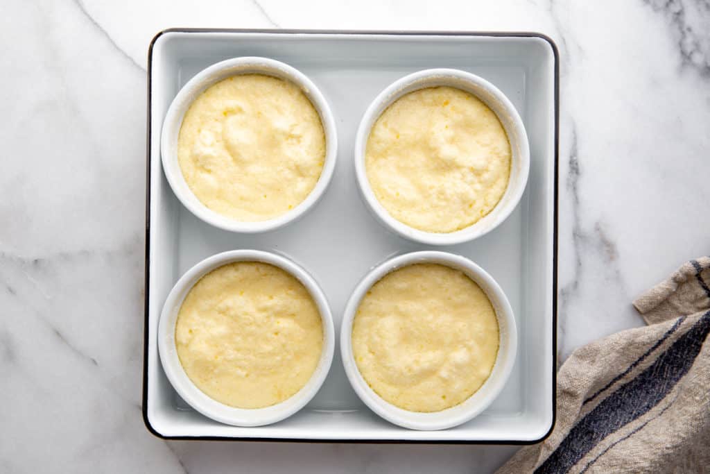 The lemon pudding cakes in a baking dish filled halfway with water.