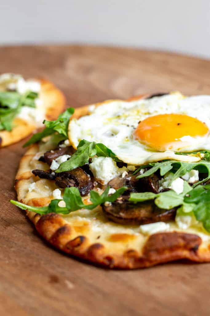 Close-up of a mushroom flatbread pizza on a wooden board.