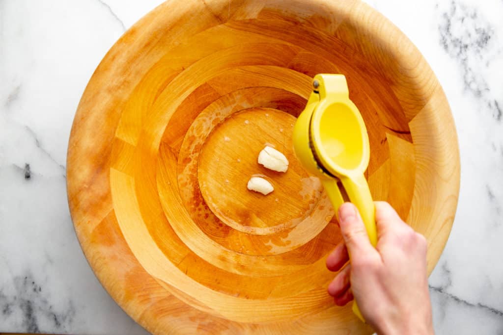 Process shot showing a hand squeezing fresh lemon juice into a salad bowl. 