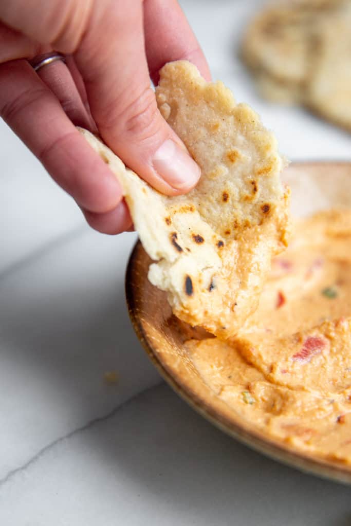 A hand dipping a torn piece of flatbread into a bowl of dip.