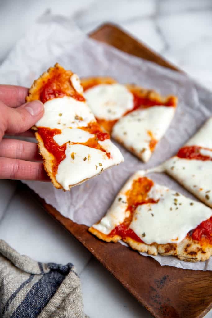 A hand holding a slice of flatbread pizza.