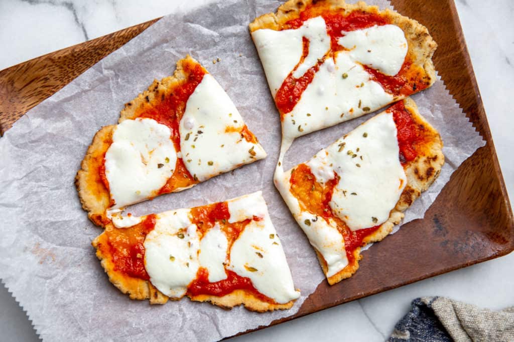 A gluten free flatbread pizza on a wooden board with parchment paper.