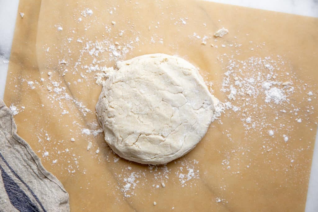 The flatbread dough in a disk on parchment paper.