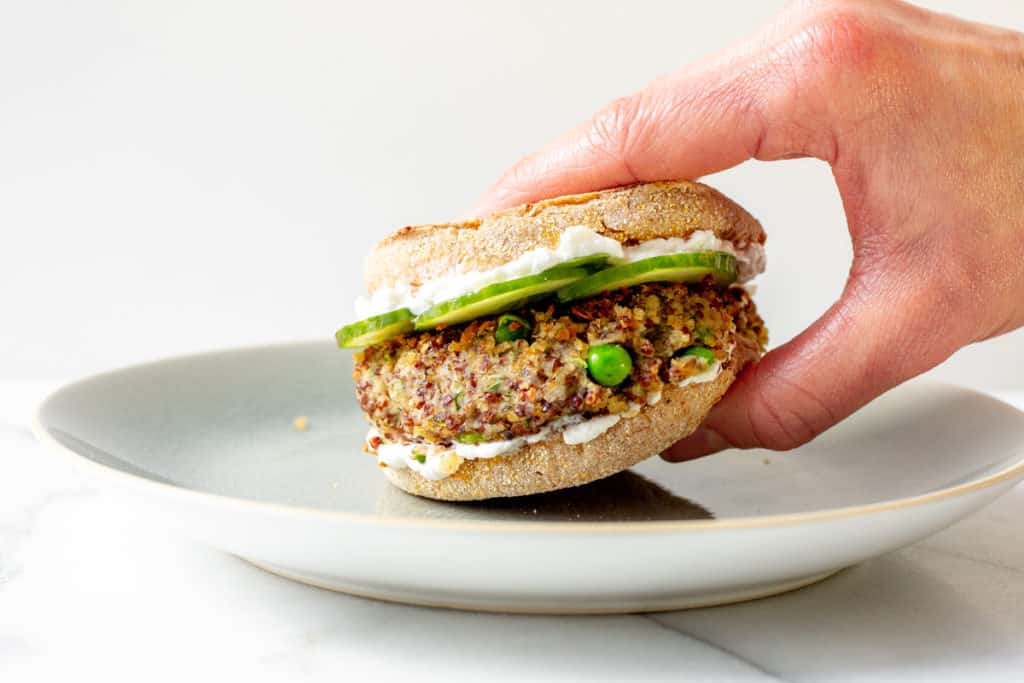 A hand grabbing a quinoa burger from a plate. 