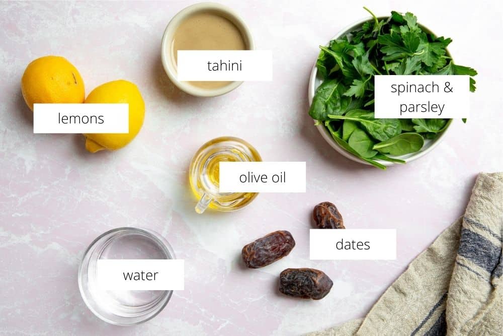 All of the ingredients for the green tahini sauce recipe arranged on a surface with labels. 