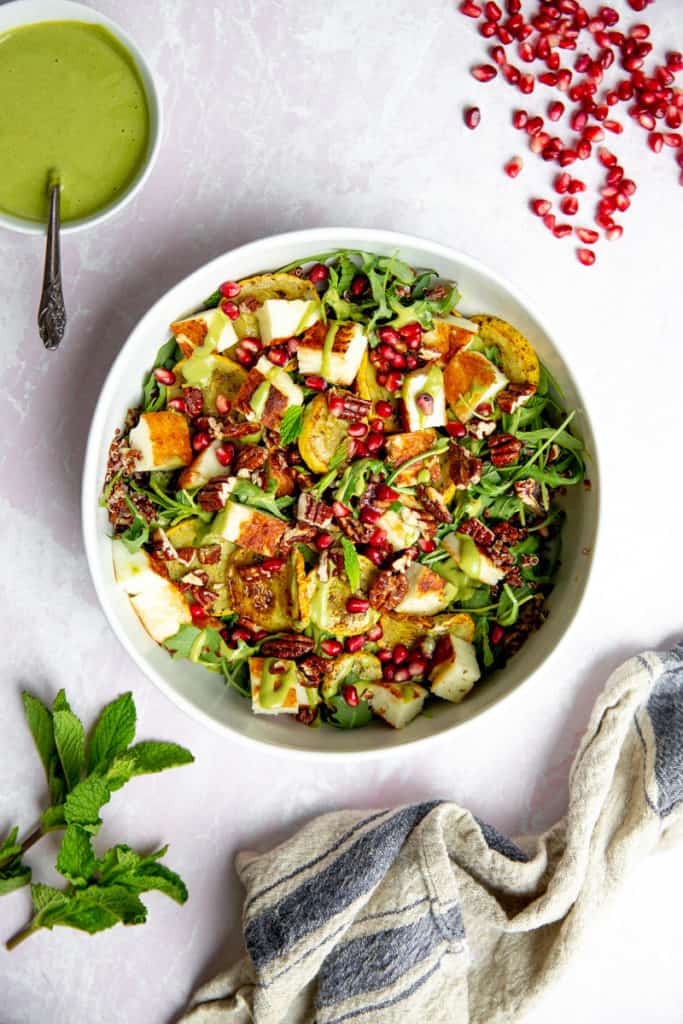 A bowl of halloumi salad drizzled with the green tahini sauce, with a small bowl of sauce alongside.