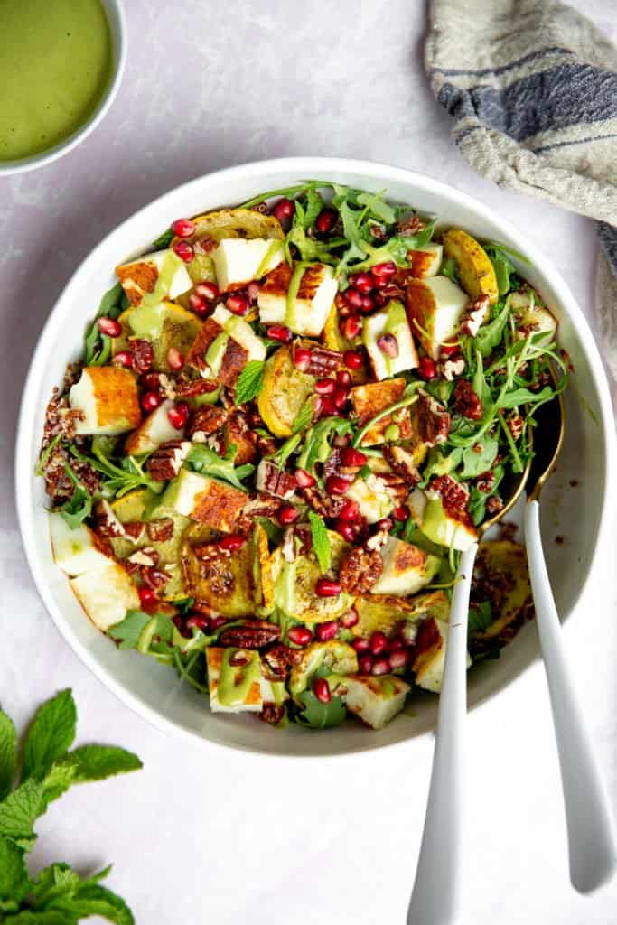 Pan fried halloumi salad in a bowl with serving spoons. 