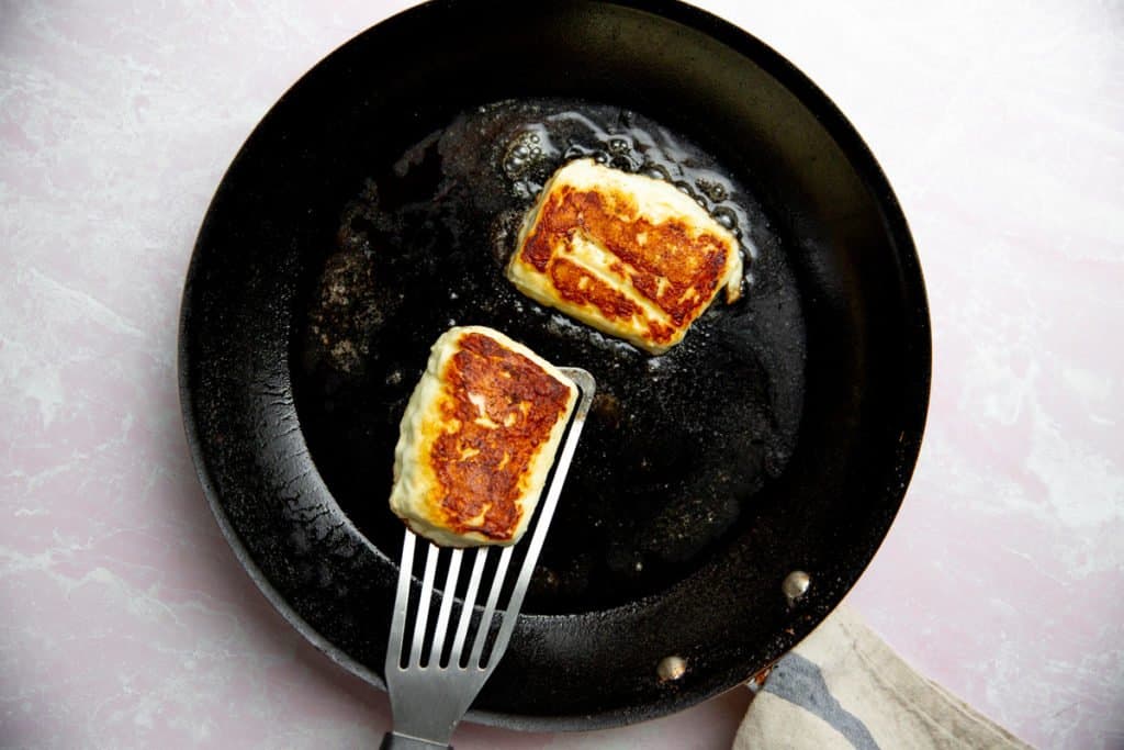 Process shot showing halloumi frying in a non-stick skillet. 
