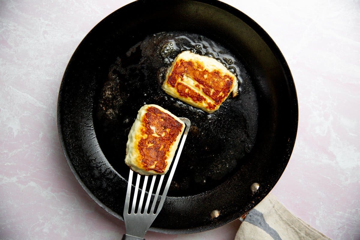 Process shot showing halloumi frying in a non-stick skillet.