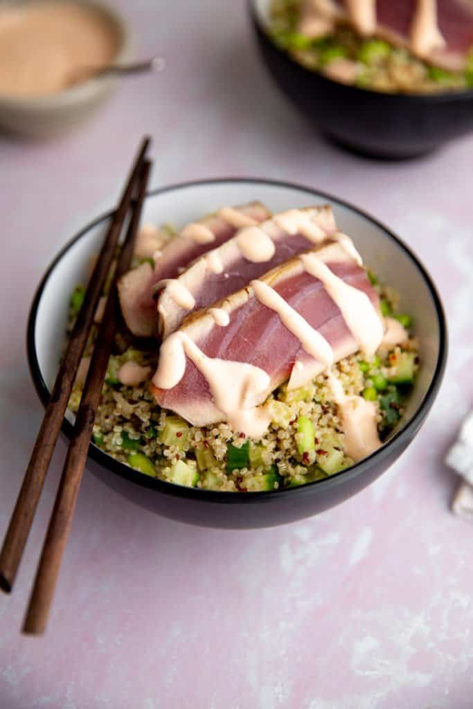 Sliced seared tuna in a bowl over edamame salad, drizzled with sriracha mayo.