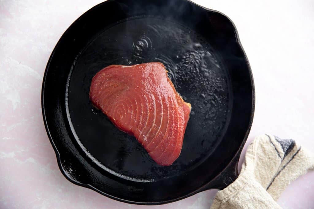 Process shot showing a tuna steak searing in a cast iron skillet.