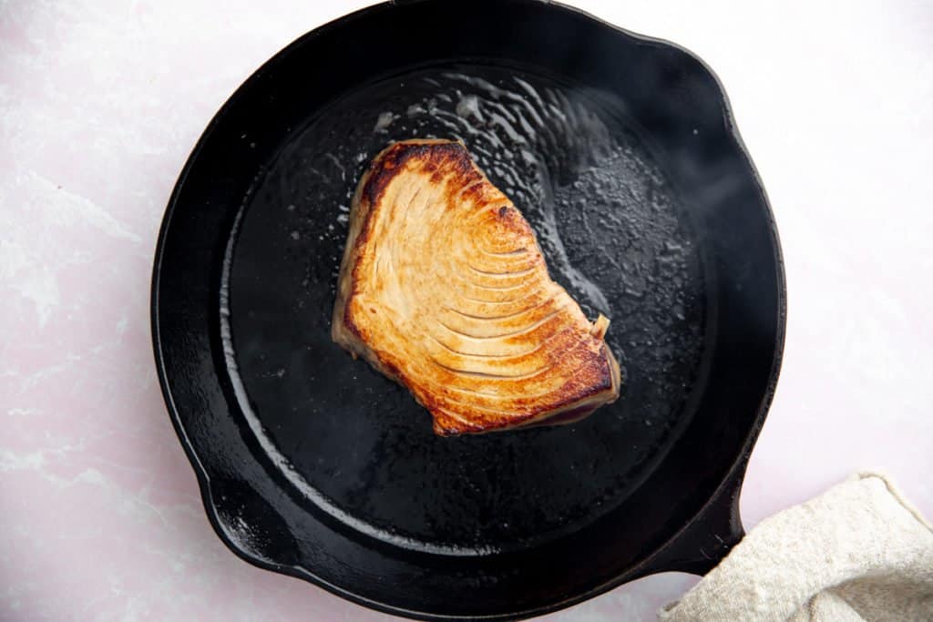 Process shot showing the cooked tuna steak in a cast iron skillet. 