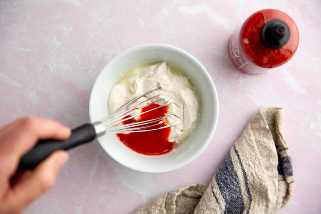 A hand whisking together the ingredients for the sriracha mayo. 