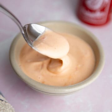 A spoon dipping into a bowl of sriracha mayo sauce.