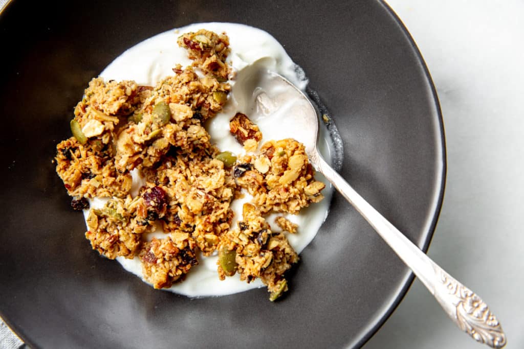 Close-up of granola clusters in a bowl with yogurt and a spoon. 