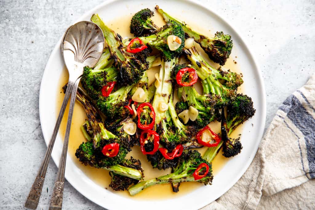 A platter of grilled broccoli with serving spoons. 