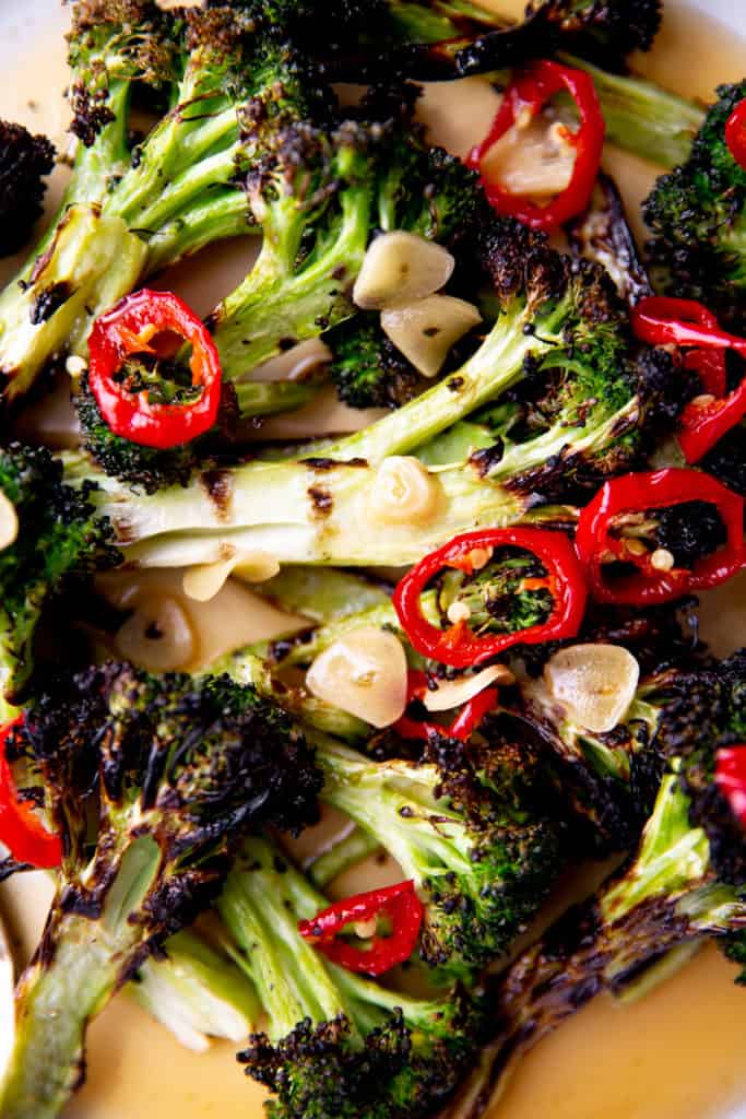 Close up of grilled broccoli on a platter topped with garlic and chiles. 