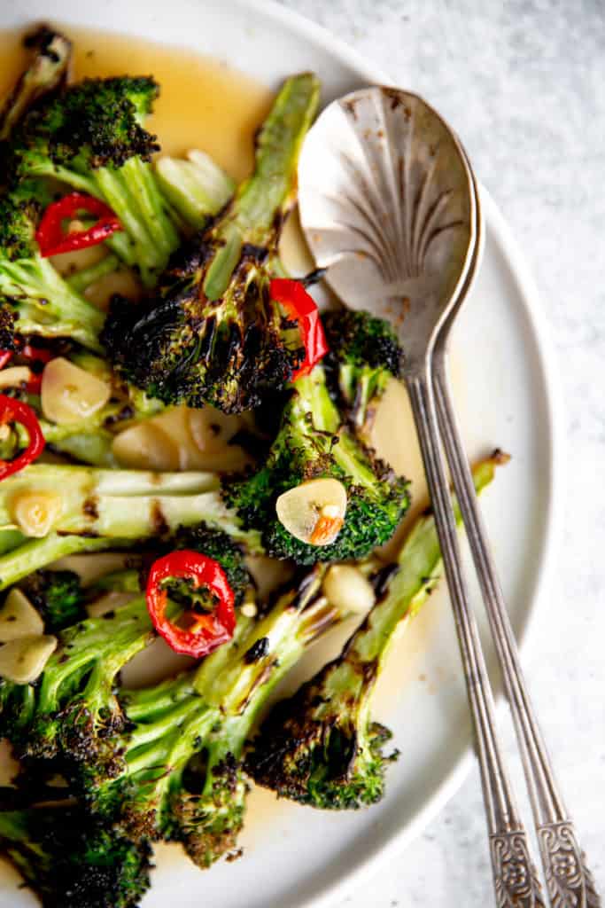 Close up of grilled broccoli on a plate with serving spoons. 