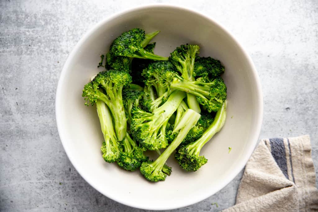 Broccoli spears in a bowl tossed with oil. 