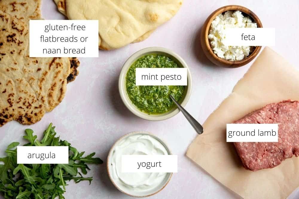 All of the ingredients for the lamb pizza recipe arranged on a surface with labels.