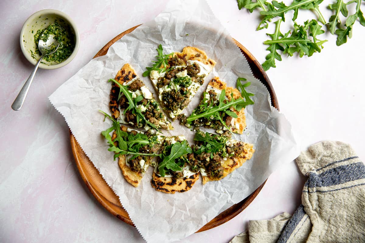 A lamb pizza on a parchment-lined wooden plate.