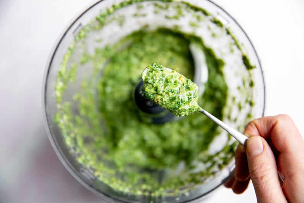A hand holding a spoonful of mint pesto. 