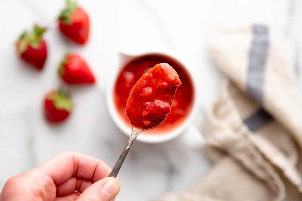 A hand holding a spoonful of strawberry sauce. 