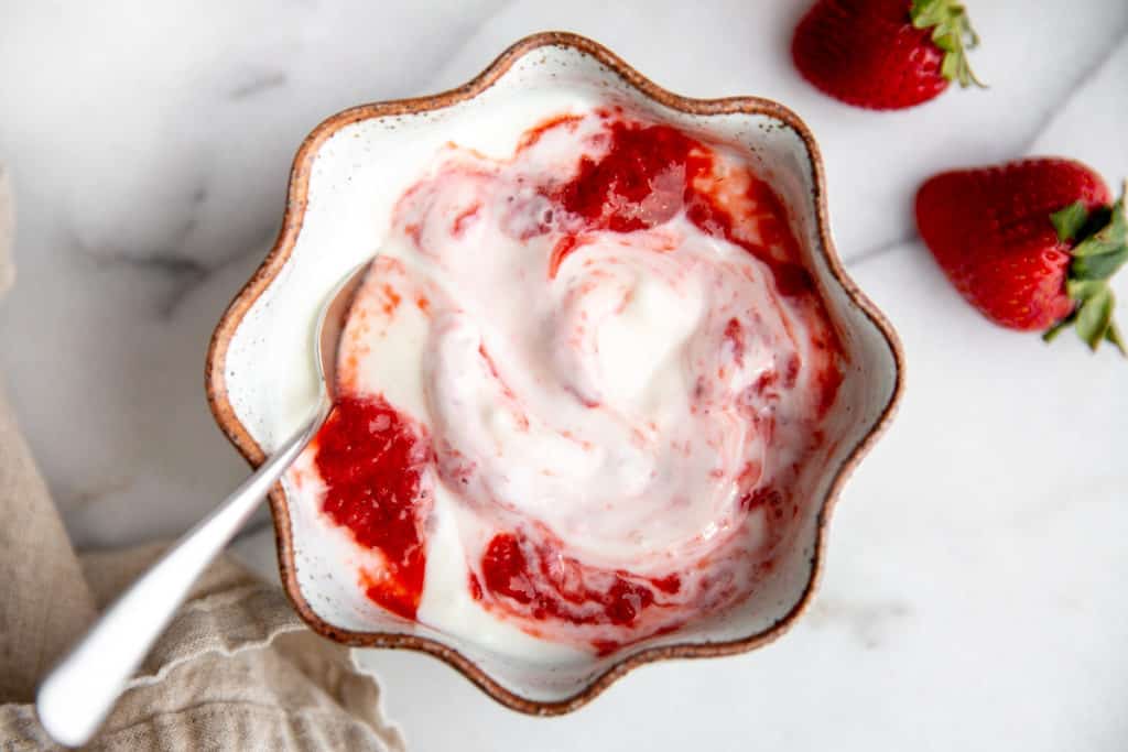 A bowl of yogurt with swirls of strawberry sauce.