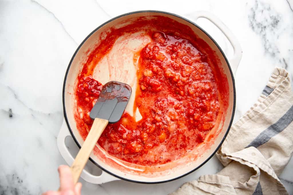 A spatula stirring the homemade strawberry sauce in a skillet, leaving a clear line along the bottom. 