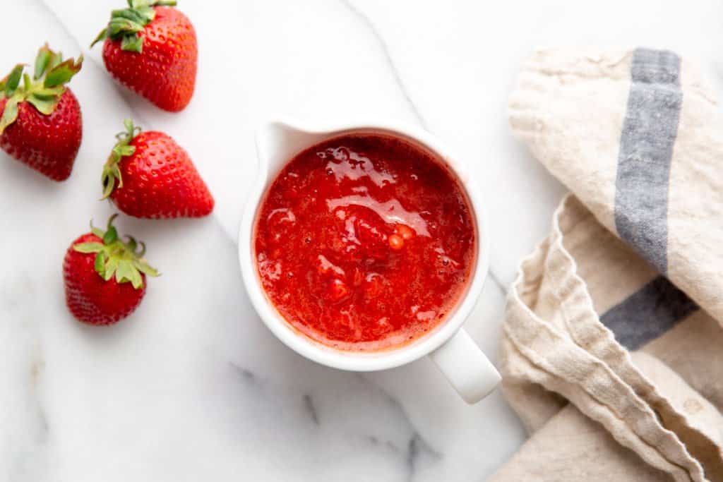 A small bowl of strawberry sauce, with fresh strawberries alongside. 