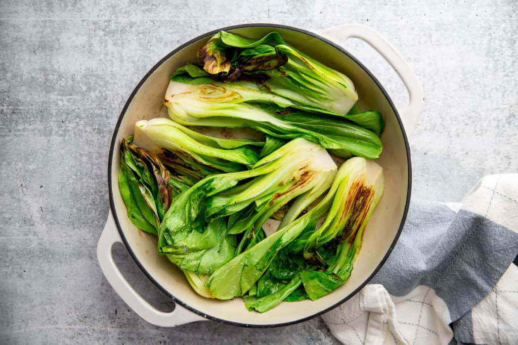 Process shot showing bok choy cooking in a large skillet. 