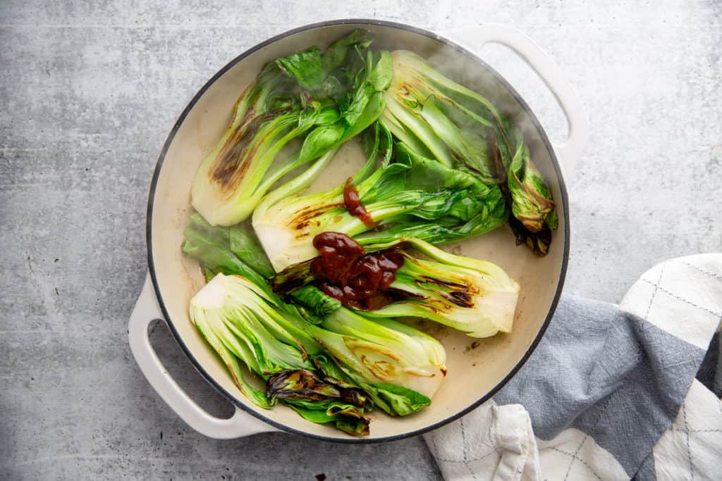 Process shot showing water and hoisin sauce being added to the baby bok choy recipe.