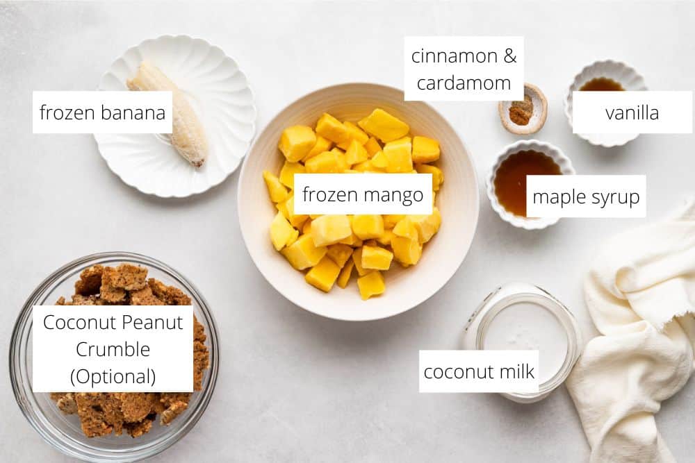 All of the ingredients for the vegan mango ice cream recipe on a white surface with labels.