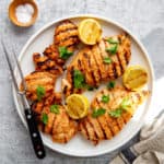 Yogurt marinated chicken pieces on a platter with grilled lemons and a serving fork.