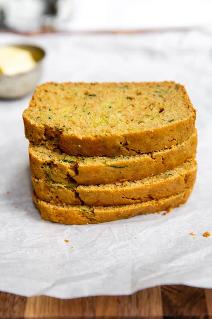Slices of zucchini bread are stacked together on top of the chopping board.