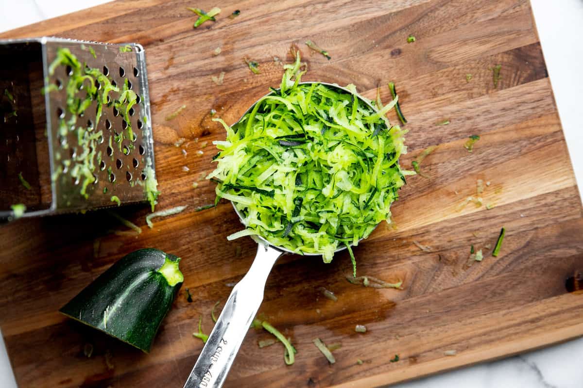 Grated zucchini in a measuring cup with a box grater alongside.