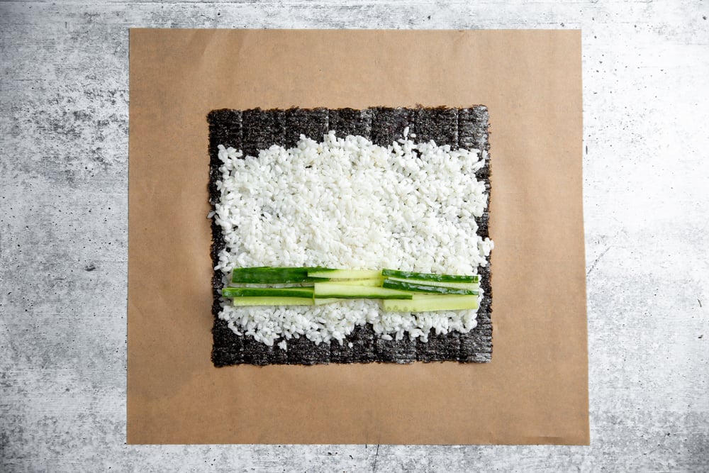 a sheet of nori filled with rice and strips of cucumbers