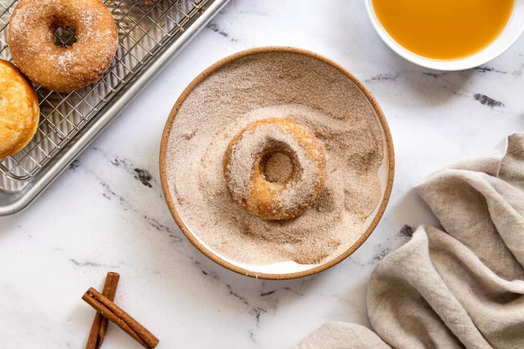 A donut in a bowl with a cinnamon sugar mixture.