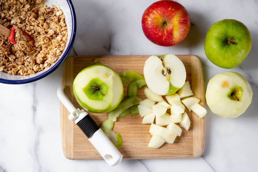 Peeled and diced apples on a cutting board with crisp topping in a bowl alongside.